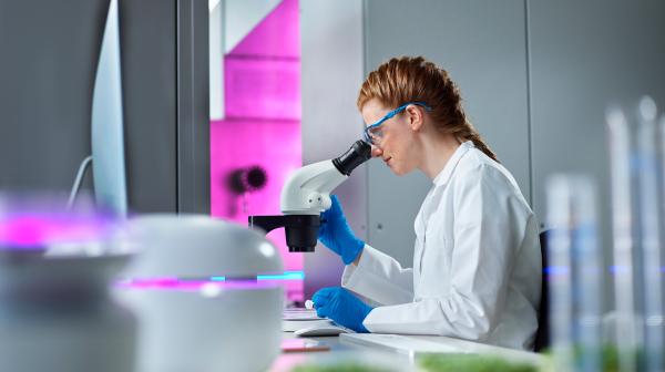 Dame im weißen Labormantel sitzt am Mikroskop