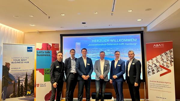 6 Personen in Anzug gekleidet stehen vor einer Leinwand