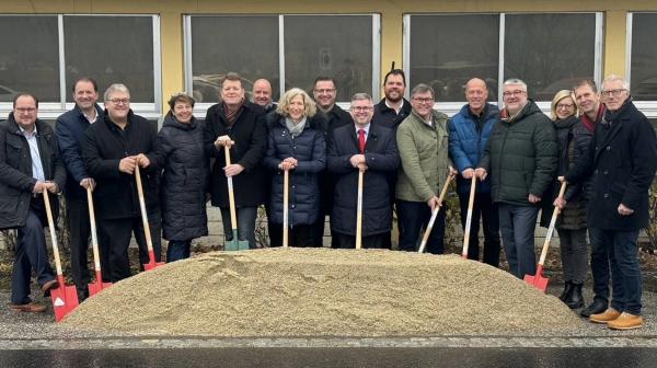 Personen stehen vor einem Gebäude mit einem Spaten