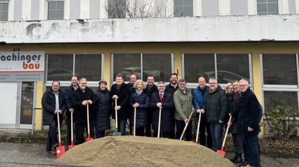 Personen stehen vor einem Gebäude mit einem Spaten