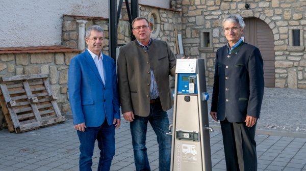 drei Personen stehen nebeneinander und präsentieren eine E Tankstelle