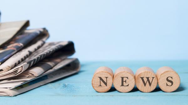 Stapel Zeitungen links und rechts kleine Holzsteine mit News-Schriftzug
