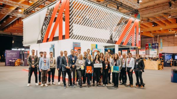 Approximately 30 people are standing in an exhibition hall in front of a booth