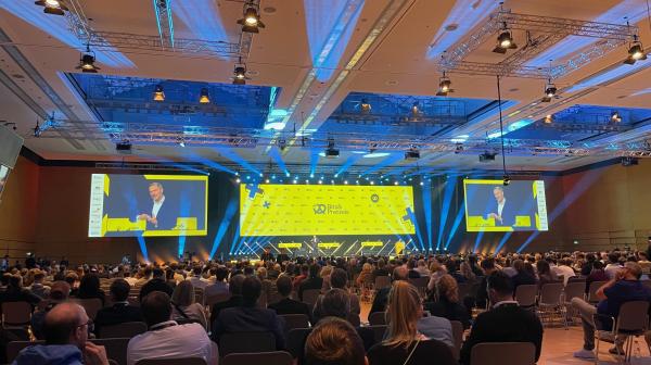 Messhalle mit großem Screen und vielen Personen auf Sesseln