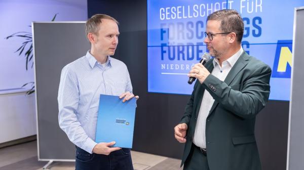 Verleihung von einer Urkunde von einem Moderator an einen Forscher