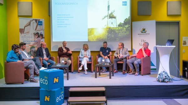 Podiumsdiskussion von 8 sitzenden Teilnehmenden auf einer Bühne