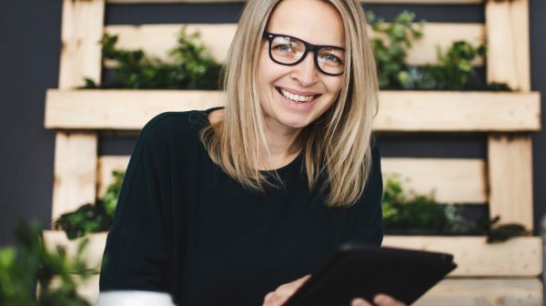 blonde Dame mit Brille mit Tablet in Händen 