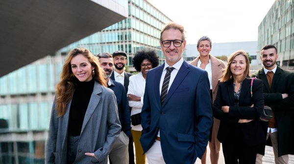 Personengruppe in Anzug steht vor modernen Bürogebäuden mit Glasfassade