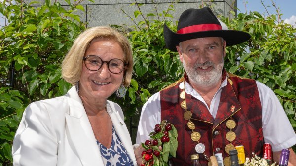 Zwei Personen bei einer Veranstaltung, eine Frau im hellen Blazer und ein Mann in Tracht mit einem Geschenkkorb