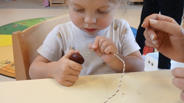 Kindergartenmädchen fädelt Kastanien auf einer Schnur auf