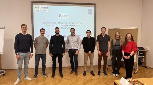 Gruppenfoto von sieben Personen vor einer Präsentation auf einer Leinwand