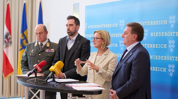 4 Personen bei einer Podiumsdiskussion vor einer Niederösterreich-Wand und drei Fahnen