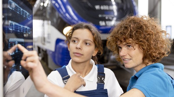 Zwei Junge Frauen in Arbeitsmontur bedienen einen Touch-Screen