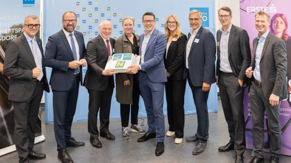 9 Personen stehen vor diversen Rückwänden und halten eine Torte