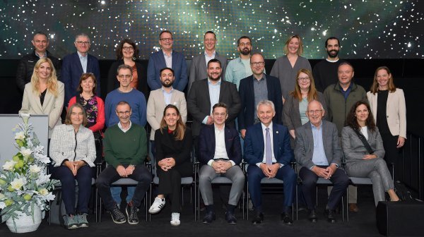 Großes Gruppenfoto von 24 Personen sitzend und stehend vor einem Sternenhintergrund