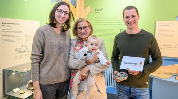 Drei Personen mit Kleinkind am Arm und Tafel Fossilienwelt