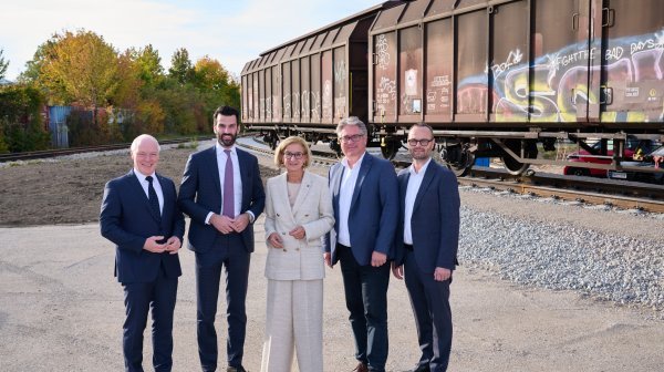 Fünf Personen vor neu verlegten Bahngleisen mit 2 Bahnwaggons im Hintergrund 