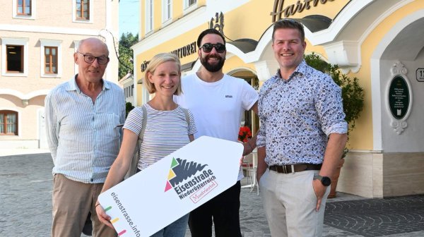 Vier Personen halten eine Eisenstraße Tafel vor einem historischen Gebäude in der Hand
