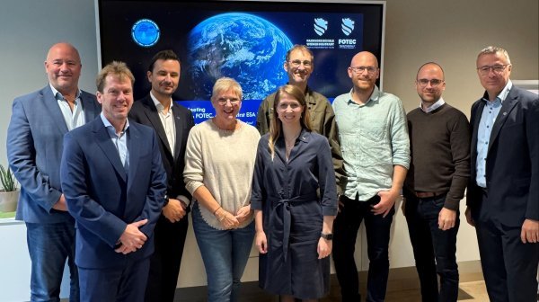 Gruppenfoto von 9 Personen vor einem großen Screen mit FH-Logos und Weltraumbild der Erde