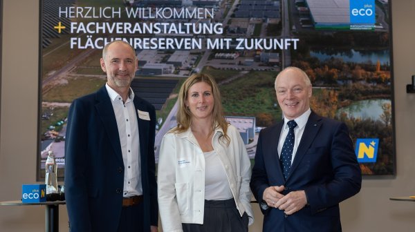 Drei Personen stehen vor einem großen Event-Screen