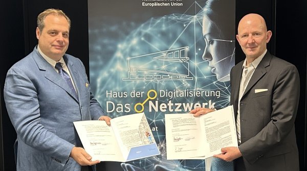 Zwei Männer stehen mit Partnerschaftsurkunden in der Hand vor einem Standsystem 
