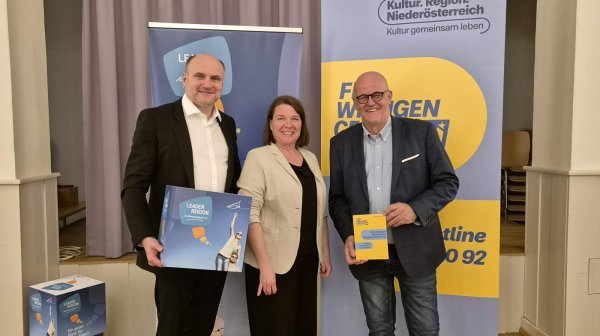 drei Personen stehen nebeneinander und halten Broschüren in die Kamera