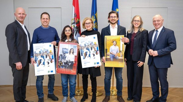 sieben Personen stehen nebeneinander und vier davon halten einen großen Kalender in der Hand