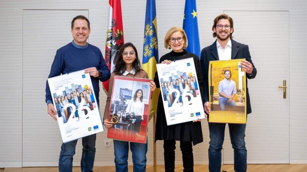 vier Personen stehen nebeneinander und halten einen großen Kalender in den Händen