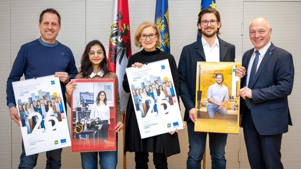 fünf Personen stehen nebeneinander und halten große Kalender in den Händen, im Hintergrund sind drei Fahnen