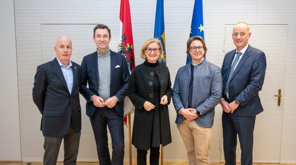 fünf Personen stehen nebeneinander im Hintergrund sind drei Flaggen zu sehen