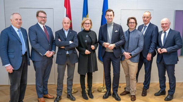 acht Personen stehen nebeneinander vor drei Flaggen