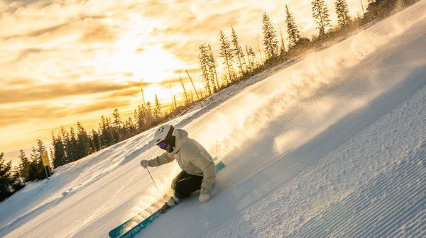 Staubender Schnee bei einem Skifahrer auf einer frisch präparierten Piste