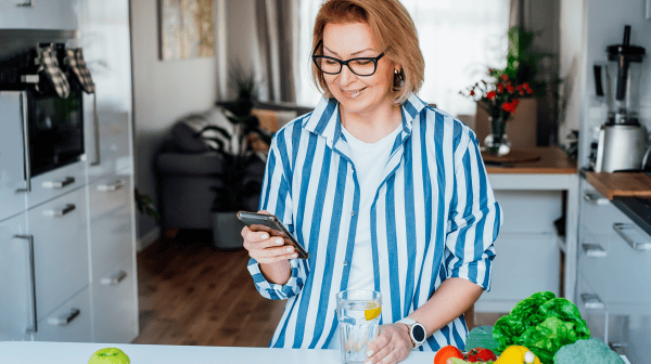 Frau am Smartphone in der Küche mit Lebensmittel auf der Arbeitsfläche