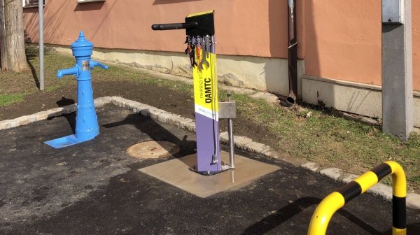 Eine blau lackierte Wassersäule und eine Fahrrad-Servicestation mit Werkzeugen an einer frisch asphaltierten Fläche.