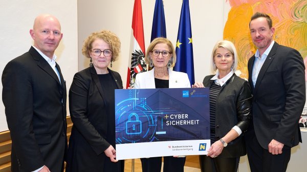 Fünf Personen stehen vor Fahne und bunten Bild mit Tafel Cyber-Sicherheit in einem Bro