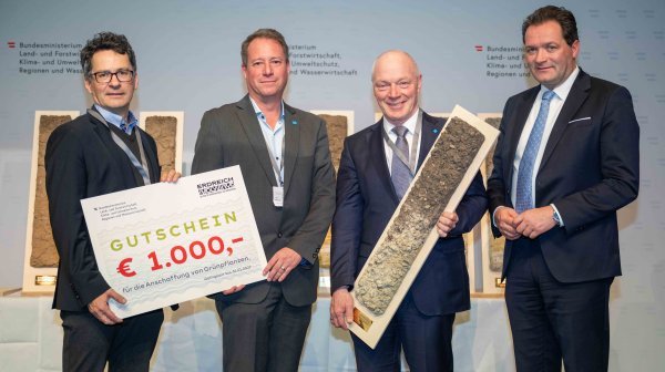 Vier Männer halten einen 1.000 € Gutschein und eine Bodenquerschnittsäule in der Hand