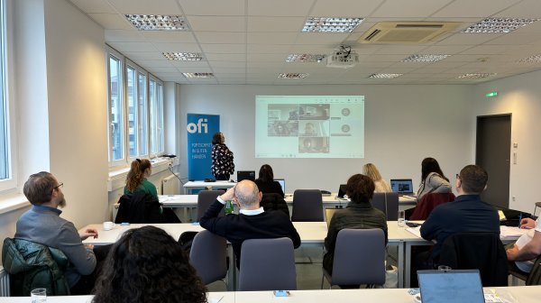 Projektmeeting - rund 10 Menschen lauschen einem Vortrag in einem Konferenzraum