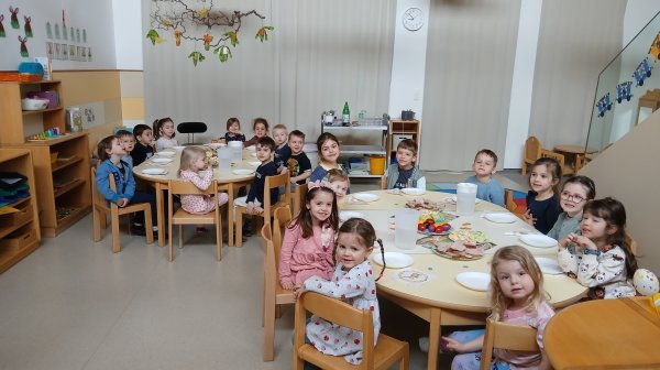 Kindergartenkinder sitzen um zwei österlich gedeckte Tische