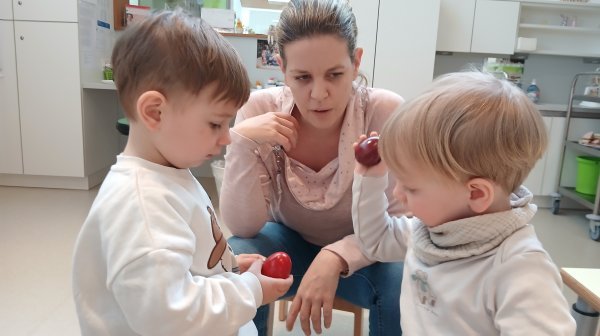 Zwei Kindergartenkinder mit einer Betreuerin beim Eierpecken