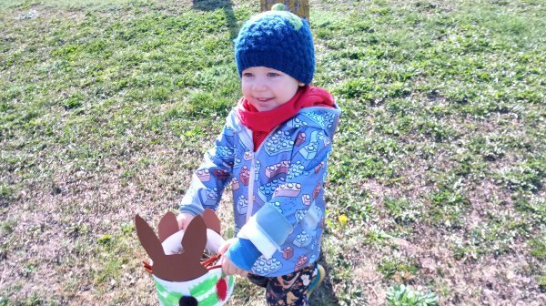 Kindergartenkind hält fröhlich ein Osternest in die Höhe