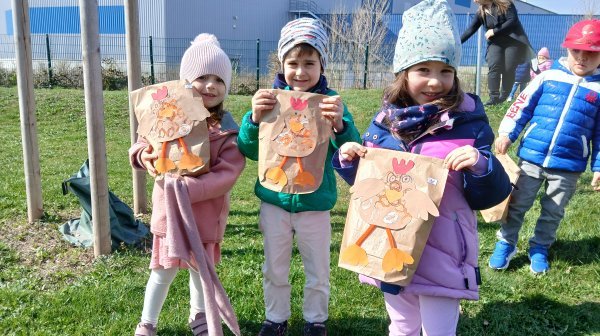 Mehrere Kindergartenkinder halten ihre verzierten Ostersackerl im Garten in die Kamera