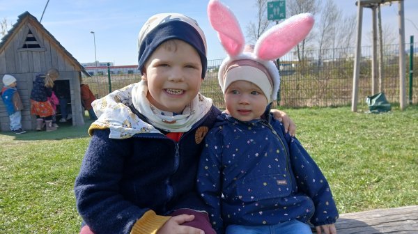 Zwei Kindergartenkinder sitzen teils mit Hasenohren im Garten des Kindergartens