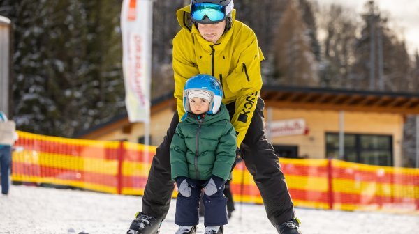 Ein Kleinkind beim Skifahren mit Unterstützung von erwachsener Person