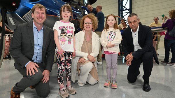 Drei Personen hockerln mit 2 Kindern neben einem kleinen Propellerflugzeug