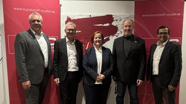 Fünf Personen stehen nebeneinander in einem Innenraum auf Holzboden.