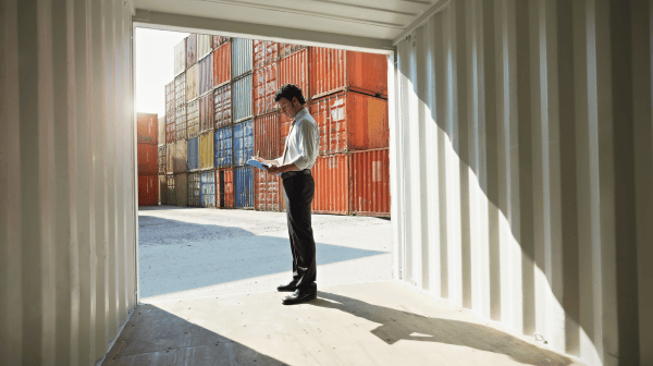 Mann mit Tablet stehend in einem offenen Schiffscontainer vor gestapelten Frachtcontainern