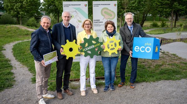 Fünf Personen stehen mit Tafel und einem ecoplus Würfel in einer Parklandschaft