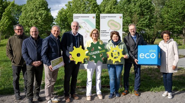 Acht Peronen stehen mit diversen Taferln und ecoplus Würfel in einer Parklandschaft