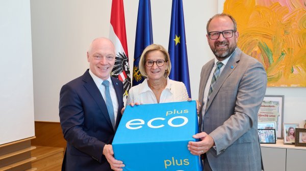 drei Personen stehen in einer Reihe und halten einen großen blauen Würfel mit der Aufschrift ecoplus in der Hand.