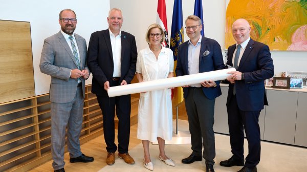 Fünf Personen stehen in einem Büro- bzw. Besprechungsraum vor den Flaggen von Österreich, Niederösterreich und der Europäischen Union.